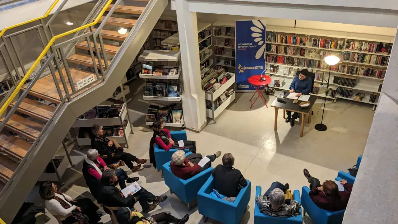 Une bibliothécaire présente un livre à un public assis. Une gestion des actifs numériques efficace permet de retrouver facilement ce type de contenu.