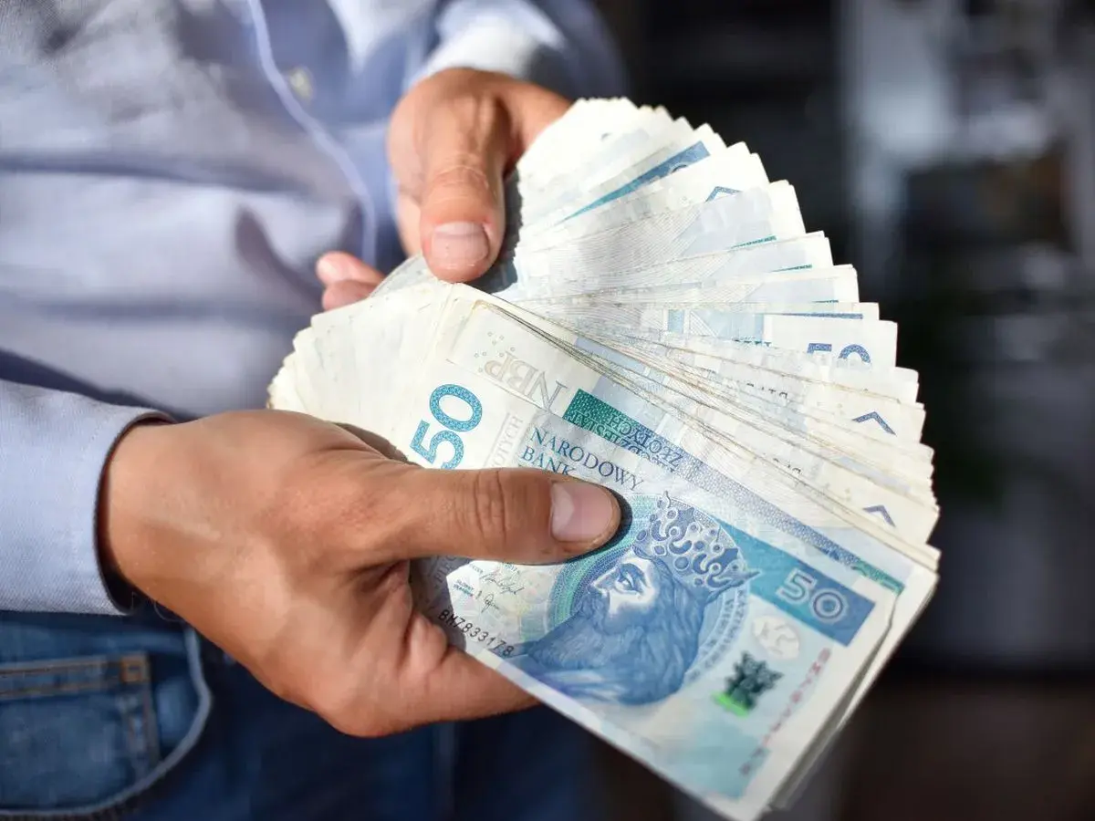 Dłonie trzymają stos banknotów 50 zł. Czy to już kwota netto?