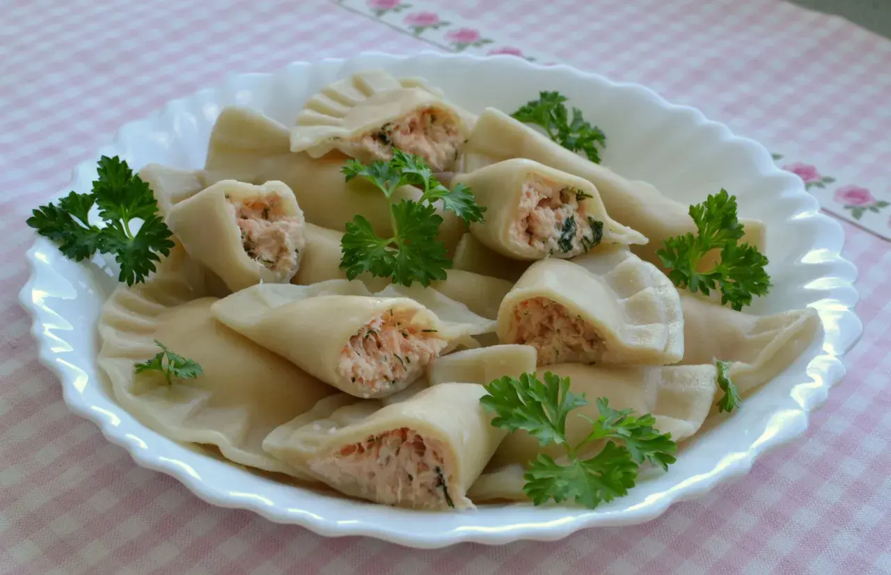 Pyszne pierogi z łososiem, delikatnie ugotowane, podane na białym talerzu z natką pietruszki.