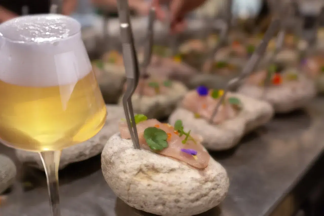 Un bicchiere di birre ale italiane accanto a tartare di pesce su pietre.