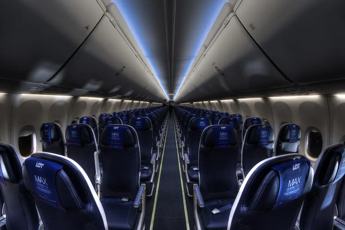 Wnętrze samolotu Boeing 737 MAX 8 LOT, rzędy ciemnych foteli z niebieskimi zagłówkami z logo LOT MAX.