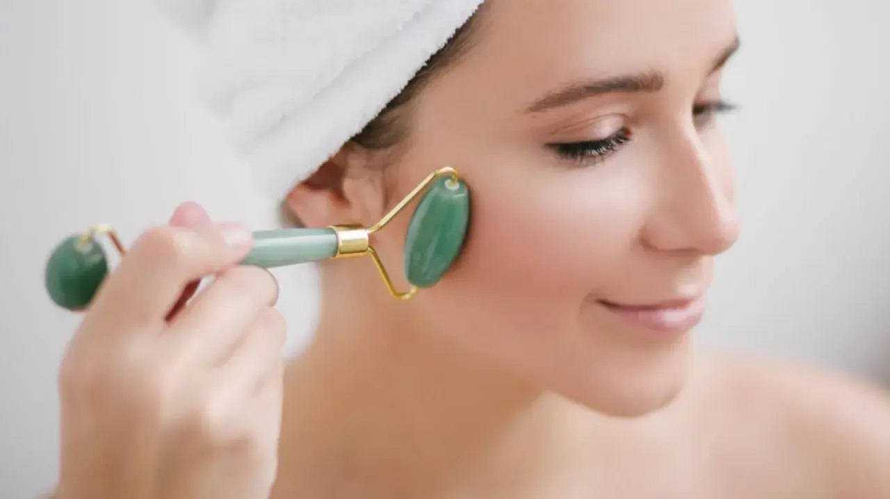 En kvinna med handduk i håret använder en grön jade roller för ansiktet.