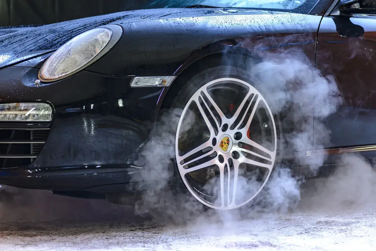 Czarny Porsche z dymem unoszącym się z koła. Sprawdź ozonowanie samochodu cennik, by odświeżyć wnętrze.