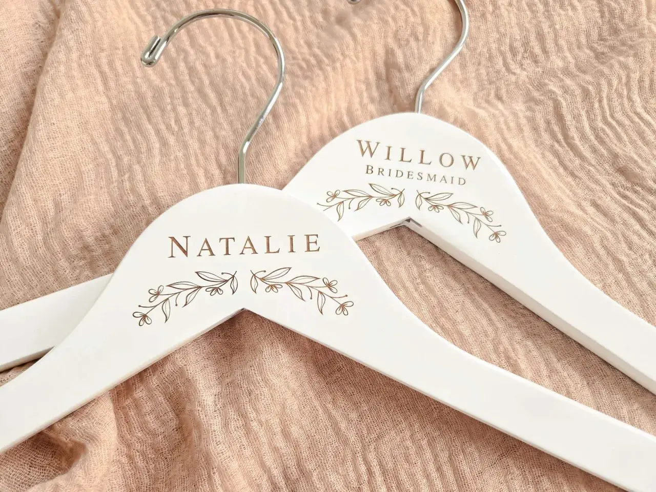 Perchas blancas personalizadas con nombres "Natalie" y "Willow Bridesmaid", adornadas con delicados motivos florales.