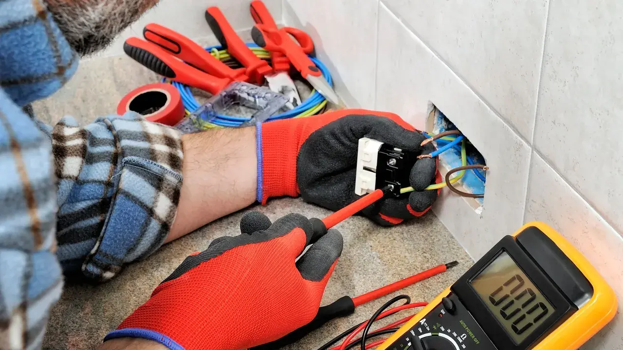 Un électricien utilise des outils pour installer une prise. On voit des fils, un tournevis, un multimètre et d'autres outils pour électricien.
