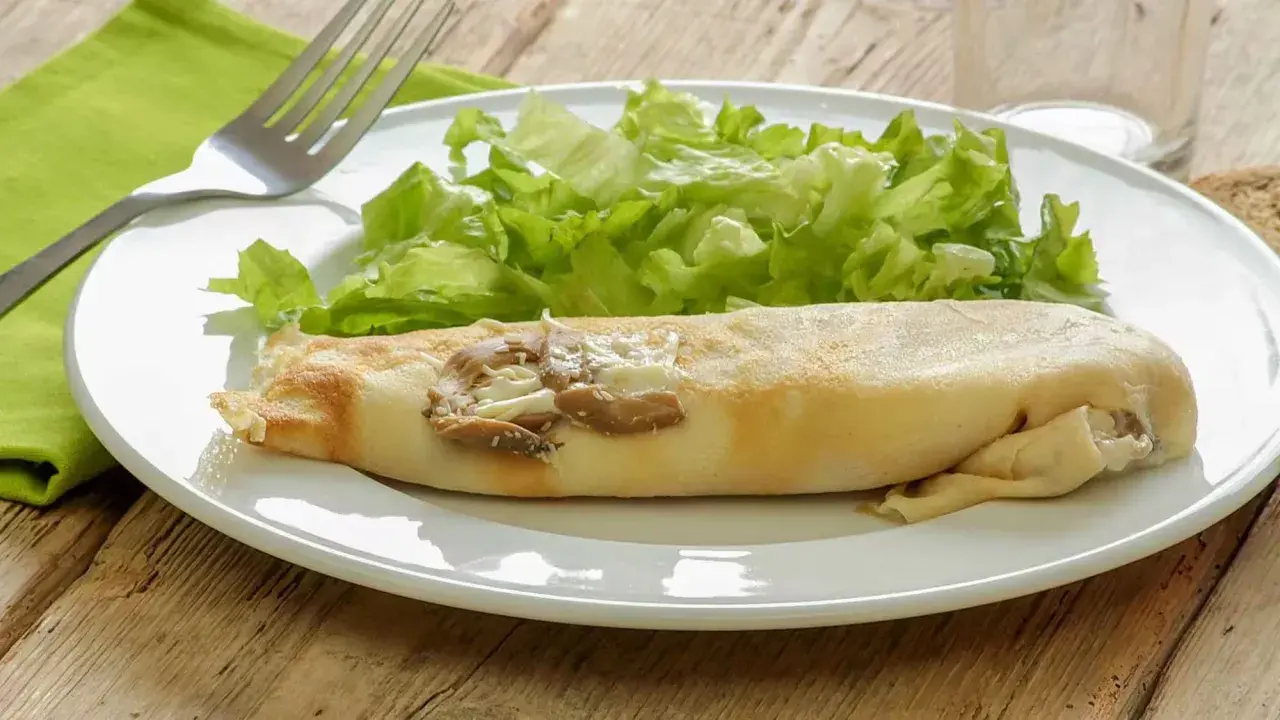 Une ficelle picarde garnie de champignons et de fromage, accompagnée d'une salade verte croquante sur une assiette blanche.