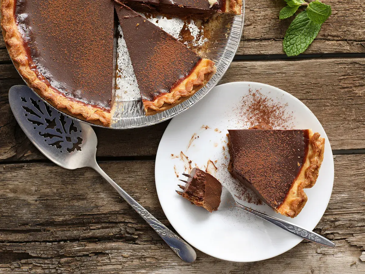 Une délicieuse tarte au chocolat, parfaite pour une recette gourmande. Une part est servie sur une assiette, prête à être dégustée.