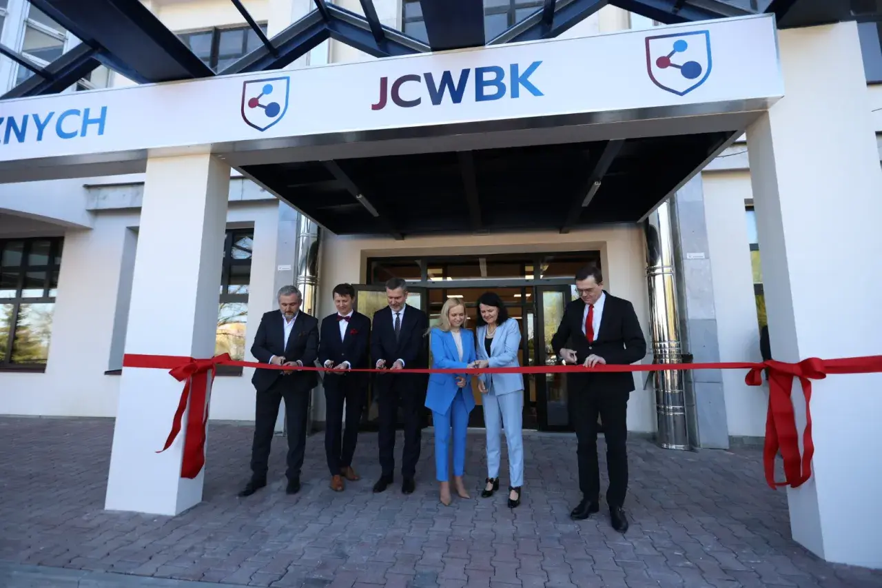Otwarcie placówki: ludzie przecinają czerwoną wstęgę przed budynkiem z logo JCWBK.