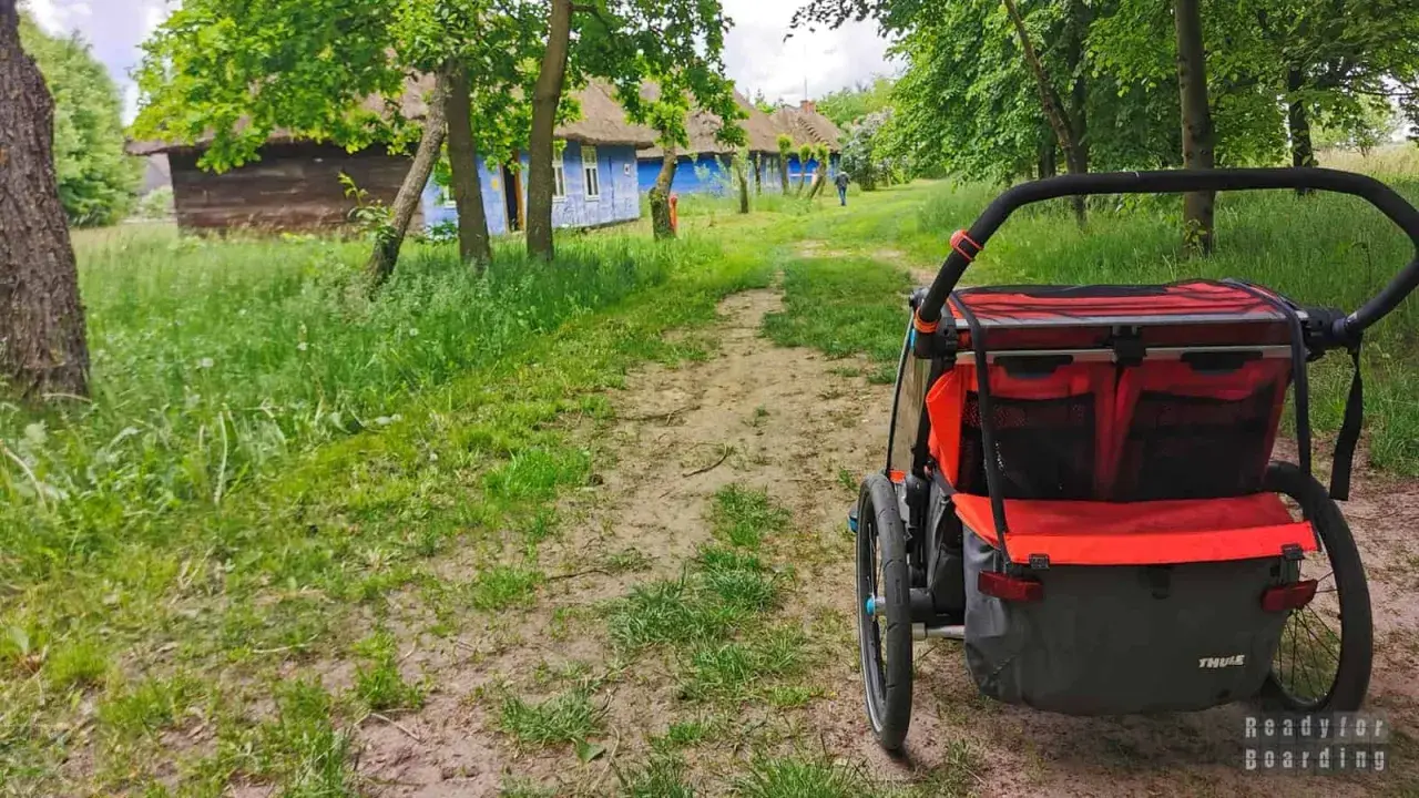 Wózek dziecięcy na tle tradycyjnych, niebieskich chat z krytymi strzechą dachami. Idealne miejsce na wycieczkę, odkrywanie ciekawych miejsc 200 km od Łodzi.