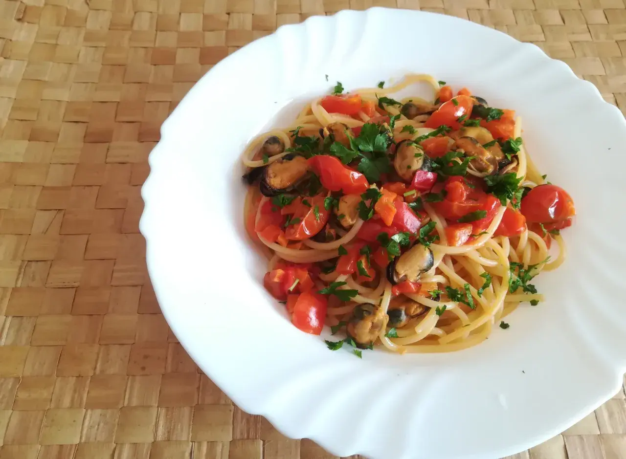 Un piatto di spaghetti con le cozze e pomodorini freschi, guarnito con prezzemolo tritato, pronto per essere gustato.