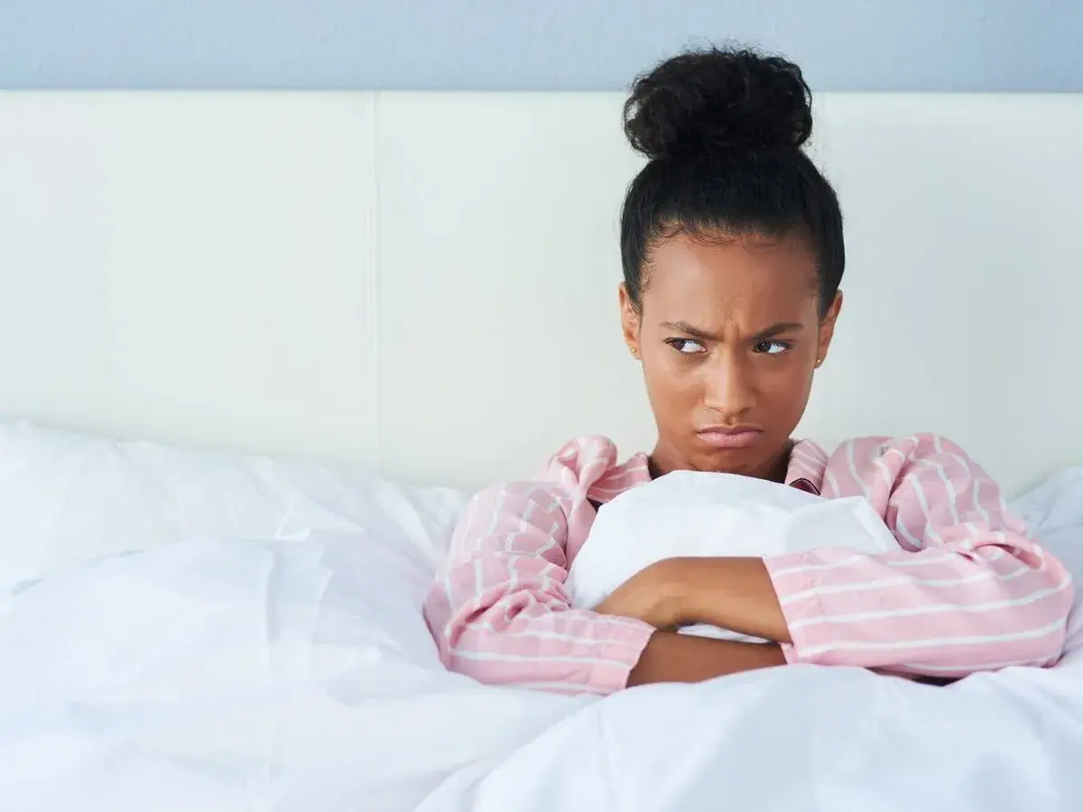 Chica enfadada en la cama, pensando en excusas para no quedar.