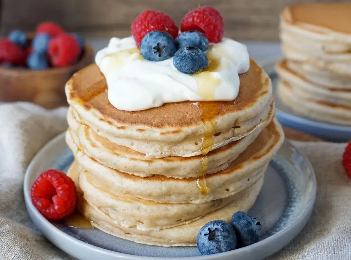 Stapel fluffiger Bananen Pancakes mit Honig, Joghurt, Himbeeren und Blaubeeren. Ein köstlicher Start in den Tag!