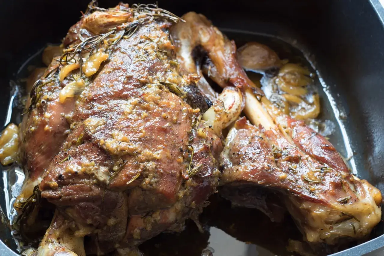 Une succulente épaule d'agneau confite, dorée et parfumée, baignant dans son jus avec des herbes et de l'ail.