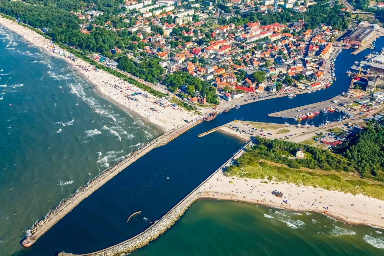 Widok z lotu ptaka na miasto i port, gdzie rzeka płynie przez Ustkę. Widać plażę, morze, falochrony i łodzie.