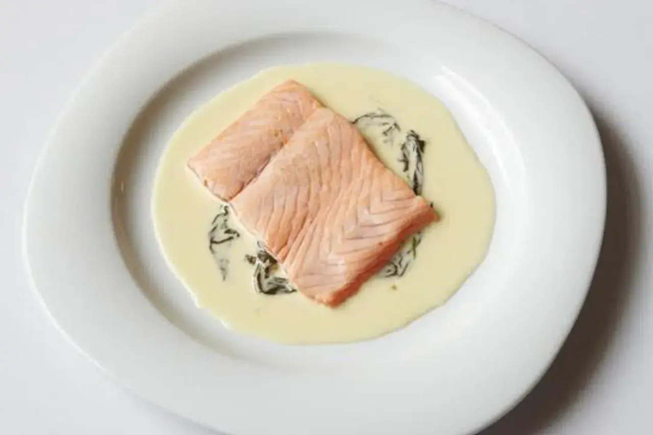 Deux pavés de saumon poêlés, nappés d'une onctueuse sauce oseille, servis sur une assiette blanche.
