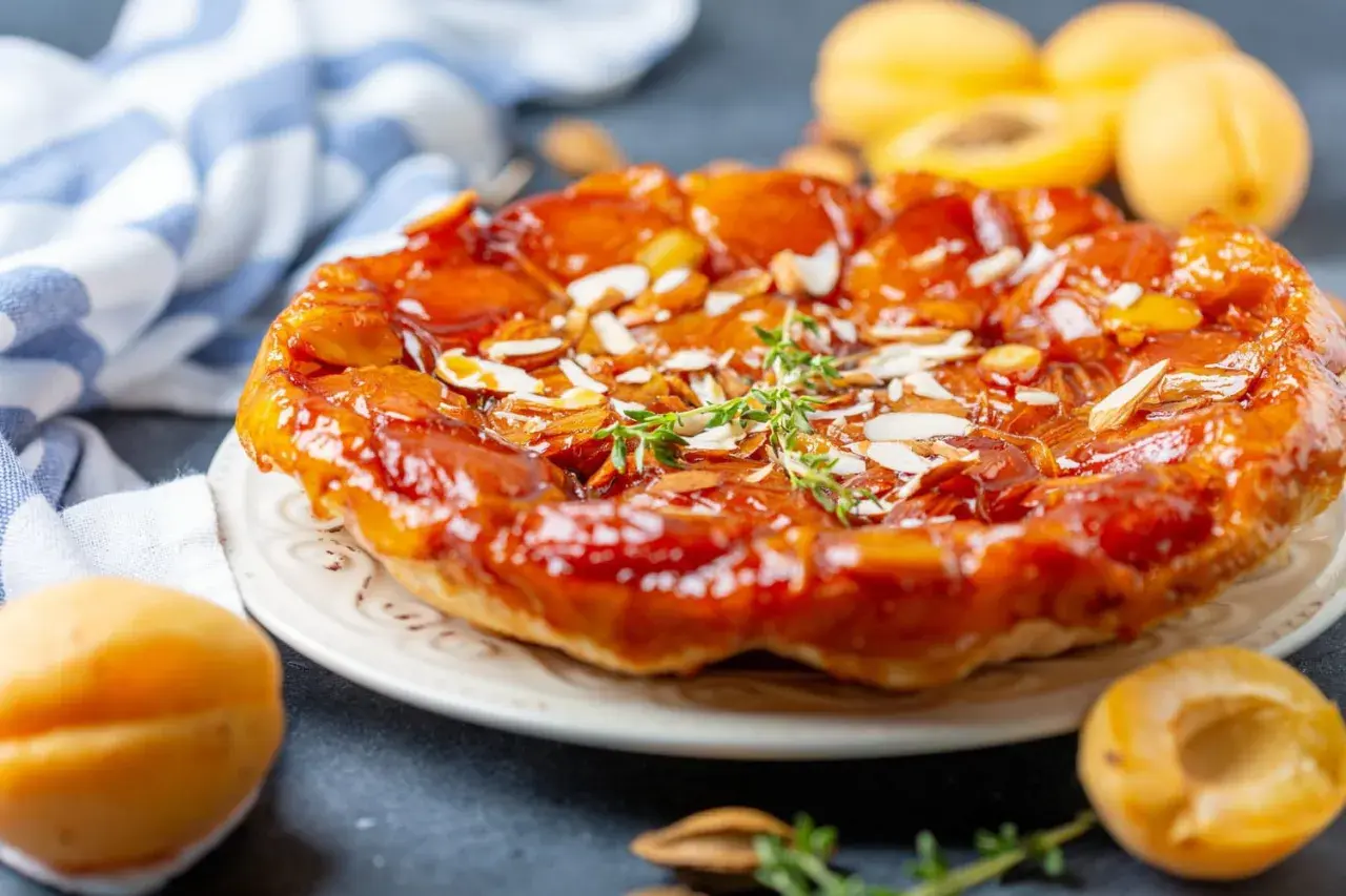 Tarte aux abricots caramélisée, garnie d'amandes effilées et d'une touche de thym frais. Un délice doré et gourmand.
