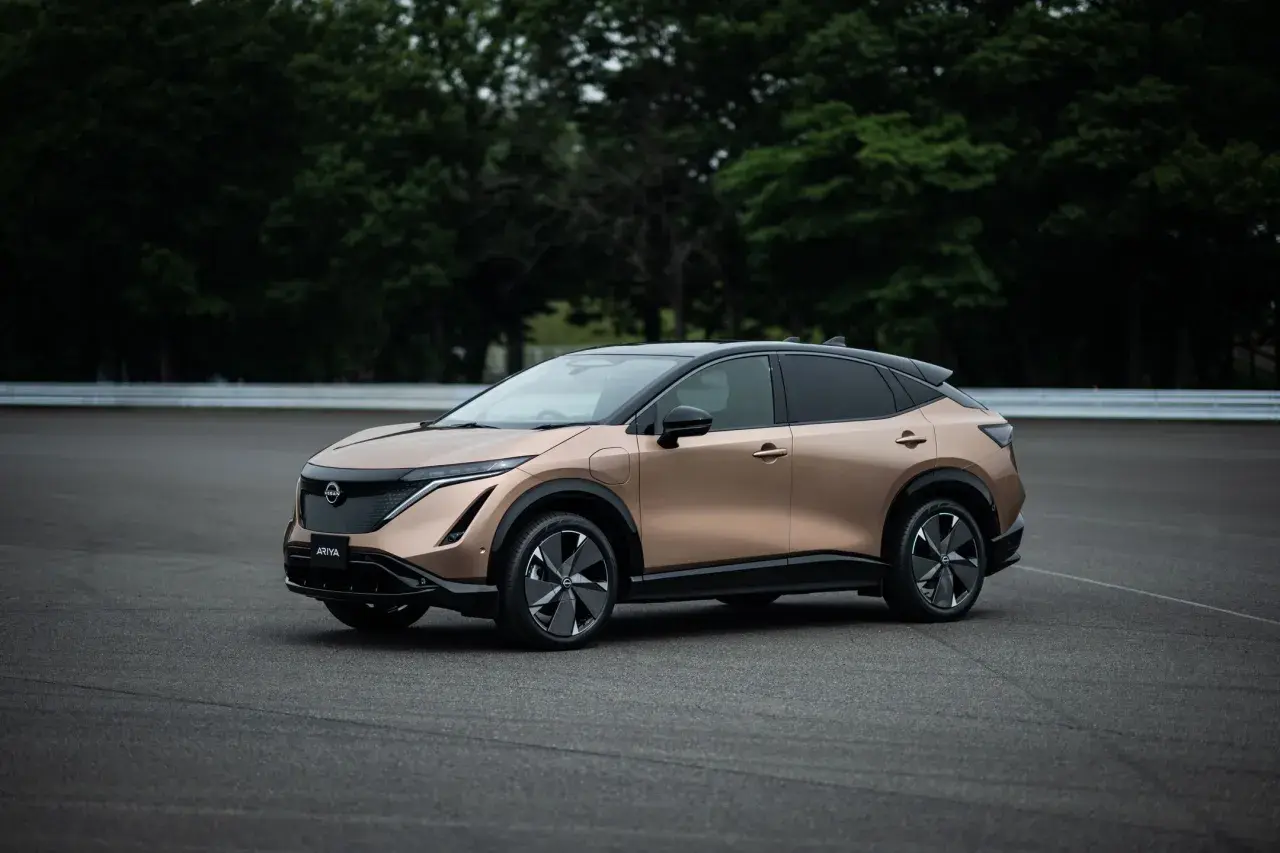 Elegancki, brązowy Nissan Ariya na tle zielonych drzew i asfaltu.