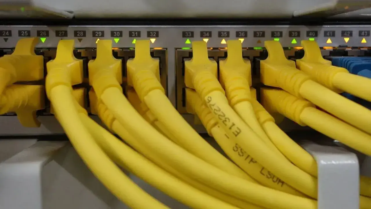 Conectores amarillos de red en un panel, cada uno con una luz verde o naranja encendida. Parece un splitter de red.