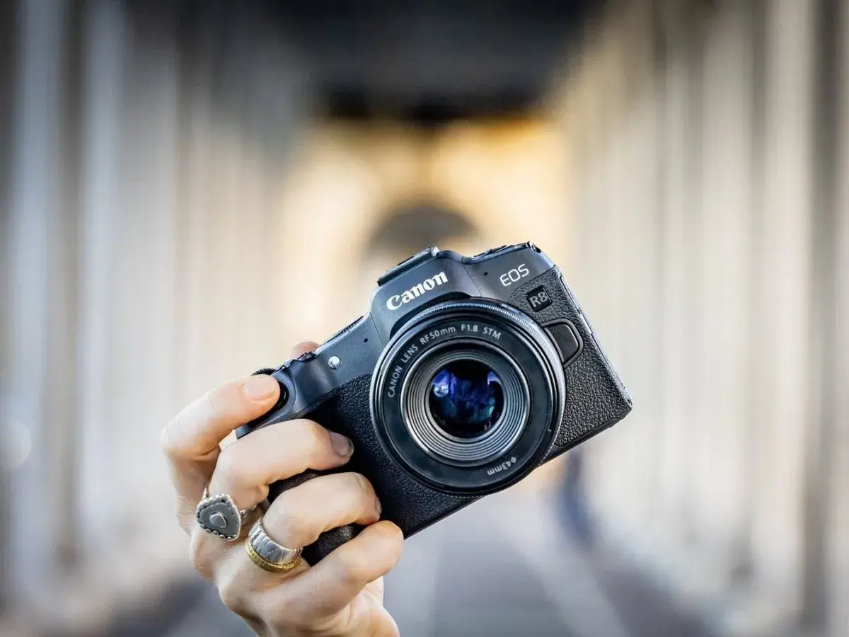 Mano che tiene una fotocamera Canon EOS R8 con obiettivo 50mm f/1.8 STM. Un modello compatto, ideale per chi cerca la qualità di un sensore canon apsc.