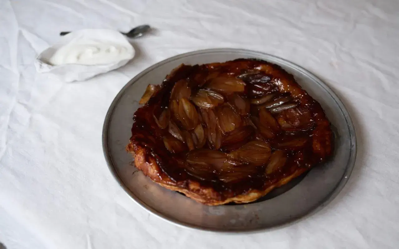 En gyllene lökpaj på en plåt, perfekt som lyxig mat att bjuda på. Serveras med en klick gräddfil.