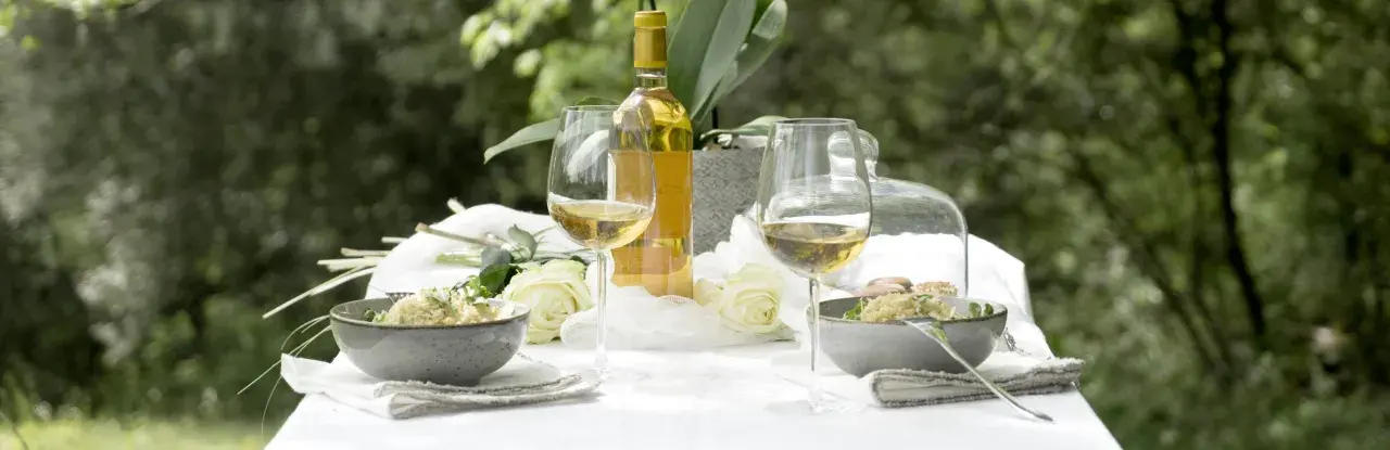 Bordeaux blanc moelleux, deux coupes de vin, deux bols de risotto et des roses blanches sur une table dressée en extérieur.