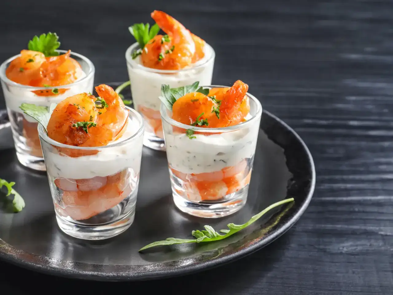 Quatre verrines apéro garnies de crevettes et d'une crème onctueuse, décorées de persil frais.