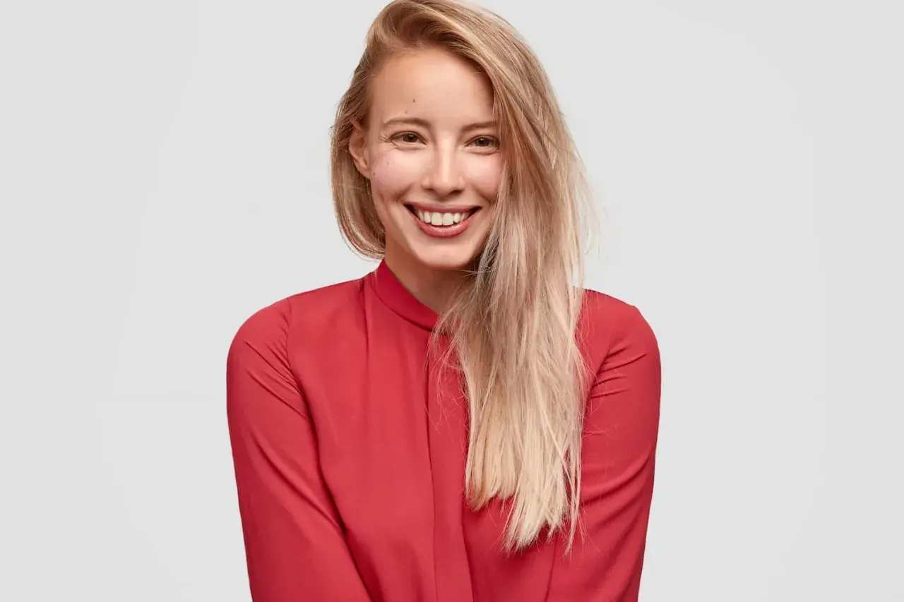Uśmiechnięta blondynka w czerwonej bluzce. Czy toner się wyplukuje? Jej włosy są jasne i lekko potargane.
