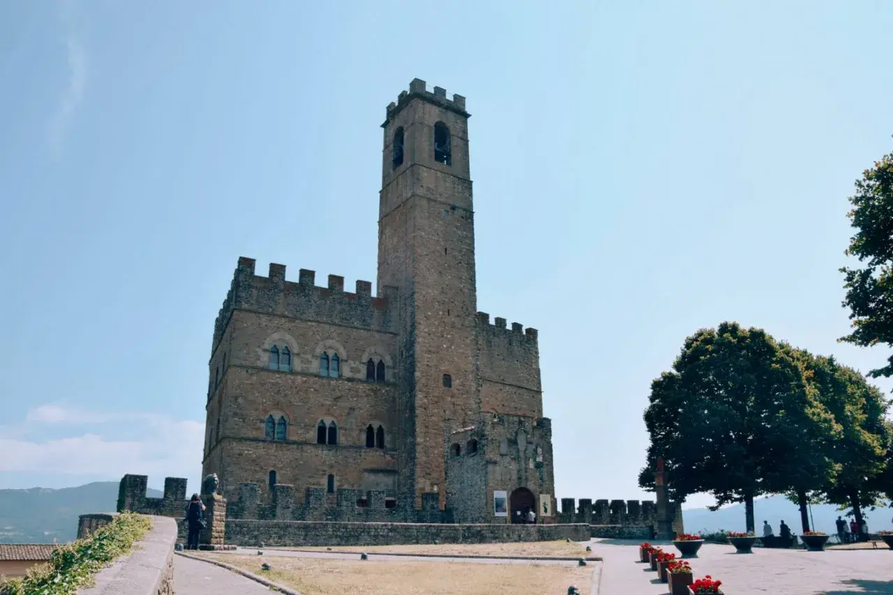 Un antico borgo alla collina domina il paesaggio, con un imponente torrione che svetta verso il cielo azzurro.