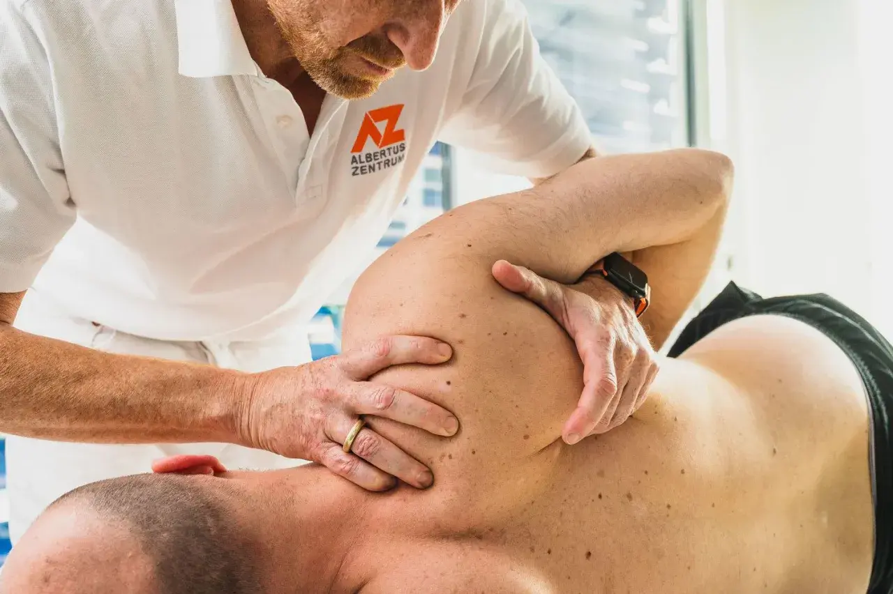 Osteopath behandelt Schulterschmerzen. Hände des Therapeuten am Schulterblatt eines Patienten.