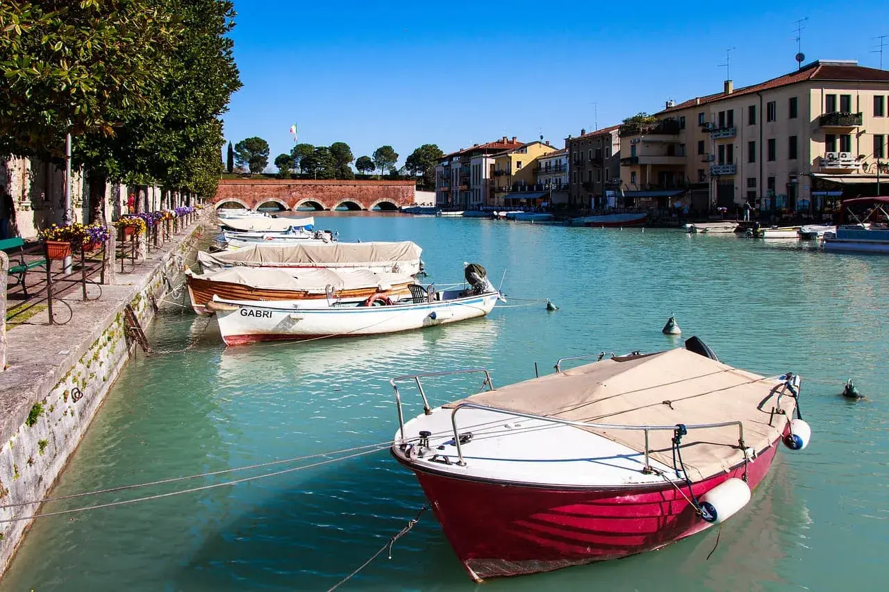 Barche ormeggiate nel canale, un assaggio di cosa vedere a Peschiera del Garda. Edifici colorati e un ponte ad arcate sullo sfondo.