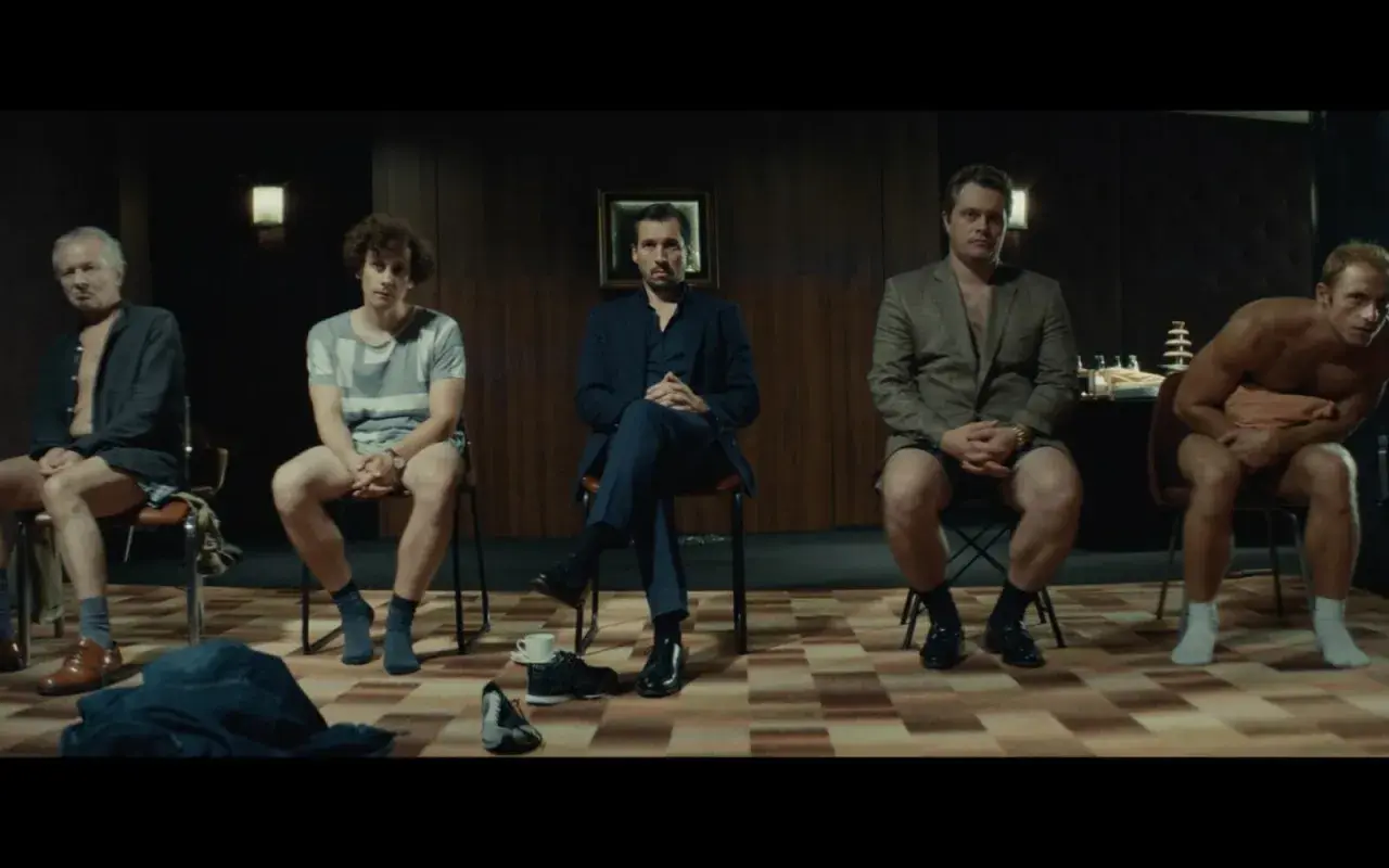 Pięciu mężczyzn siedzi na krzesłach, każdy w innym stroju. Scena z filmu "samiec alfa".