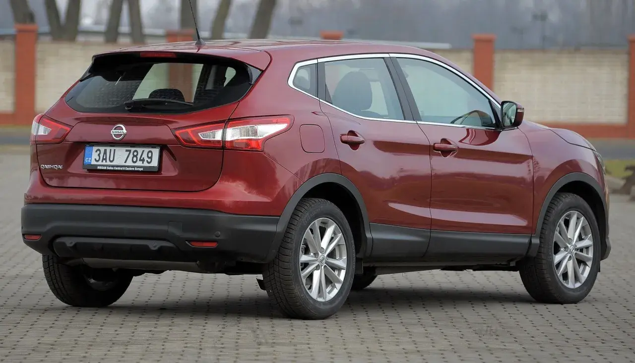 Czerwony Nissan Qashqai 2015 z czeskimi tablicami rejestracyjnymi stoi na brukowanym placu.