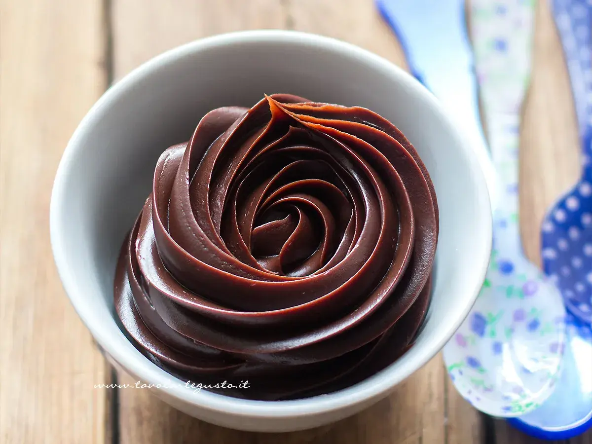 Una spirale di ganache cioccolato per copertura, lucida e invitante, in una ciotola bianca.