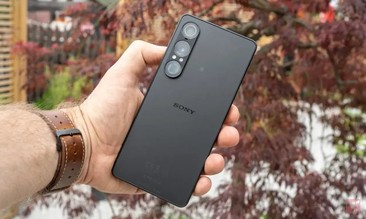 Czarny smartfon marki Sony z potrójnym aparatem, trzymany w dłoni na tle jesiennych liści.