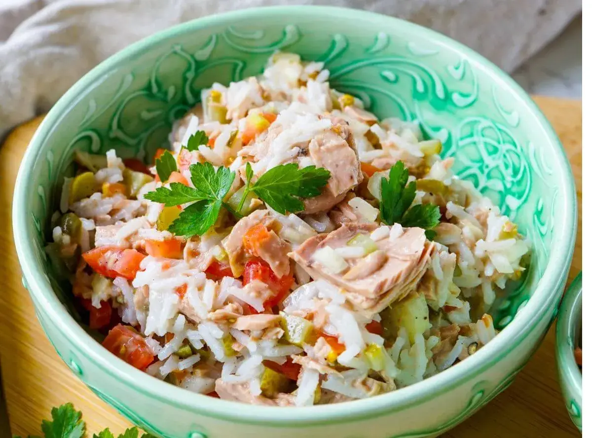 Reissalat mit Thunfisch, Tomaten und Gurken, garniert mit Petersilie, in einer grünen Schüssel.