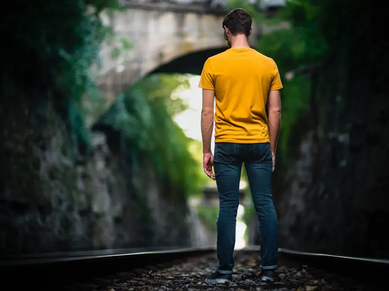 Man op spoor, omringd door groen. Een metafoor voor het navigeren door het leven met hsp, waar elke stap bewust gezet moet worden.