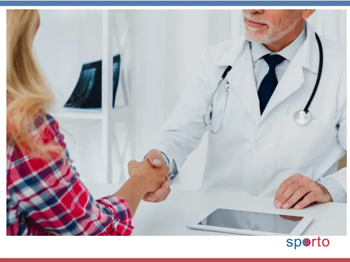 Lekarz specjalista w białym kitlu wita pacjentkę uściskiem dłoni. Rozpoczyna się zmiana lekarza specjalisty w trakcie leczenia.