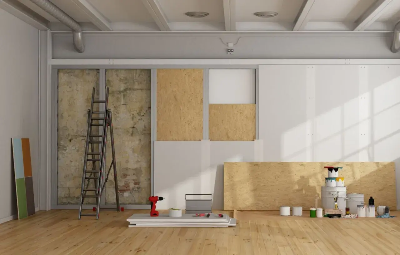 Chantier de rénovation avec panneaux de bois, échelle, outils et pots de peinture.
