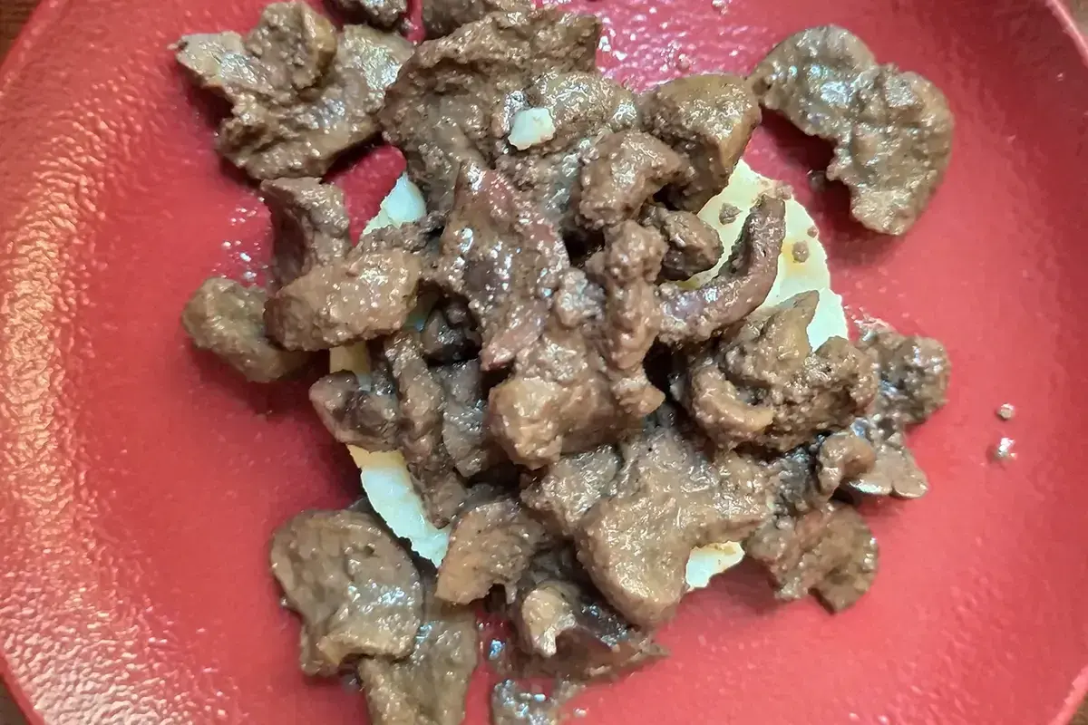 Un succulento piatto di frittura di maiale, servito su una base di patate, su un piatto rosso.