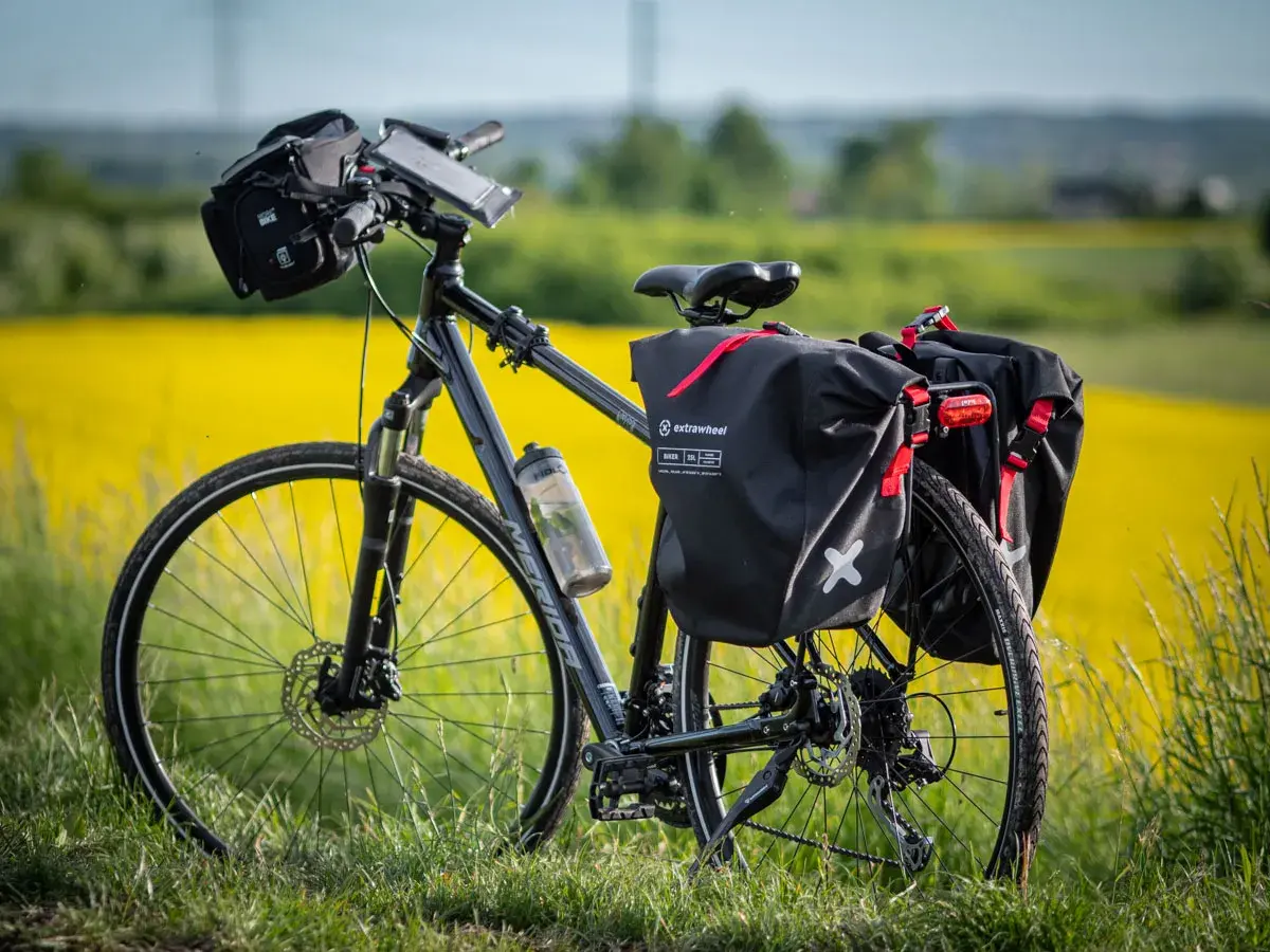 Rower z sakwami Extrawheel gotowy na wyprawę. Jakie sakwy rowerowe wybrać na długą trasę? Te czarne, wodoodporne, z czerwonymi akcentami, wyglądają na solidne.