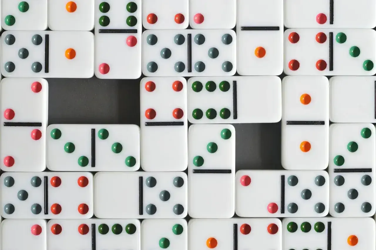 Wiele białych kostek do gry w domino z kolorowymi kropkami (zielonymi, czerwonymi, szarymi i pomarańczowymi) ułożonych w rzędy.