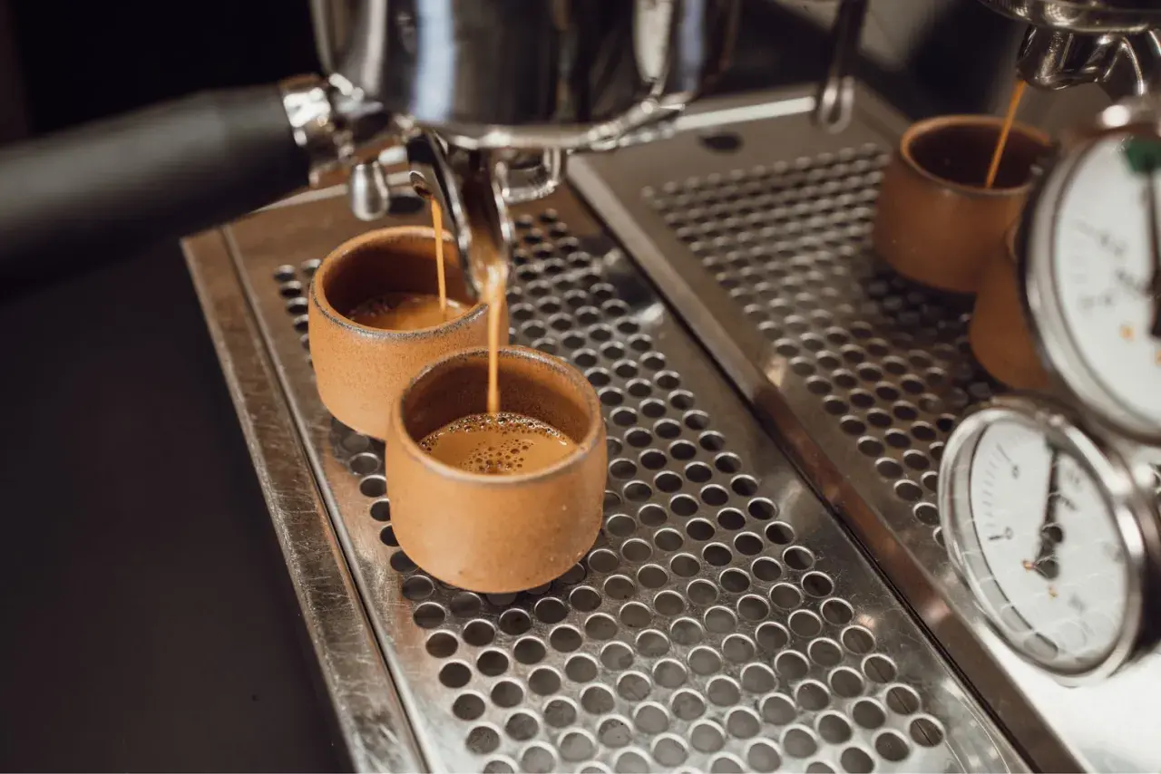 Zwei kleine Tassen werden mit Espresso gefüllt. Der Unterschied zwischen Café Crema und Kaffee Lungo wird hier deutlich: die Menge und die Crema.