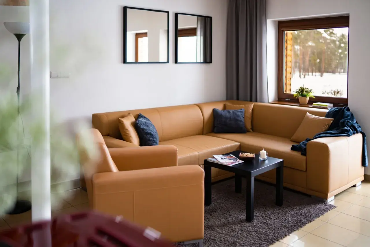 Przytulny salon z brązową kanapą i fotelem, z widokiem na zimowy las. Idealne miejsce na odpoczynek, jak w **starej wsi**.
