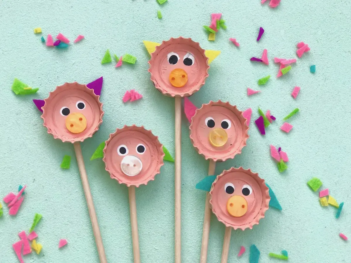 Fünf süße Schweinchen-Gesichter, gebastelt mit Kronkorken, Augen und Knöpfen. Eine tolle Idee zum Basteln mit Kronkorken!