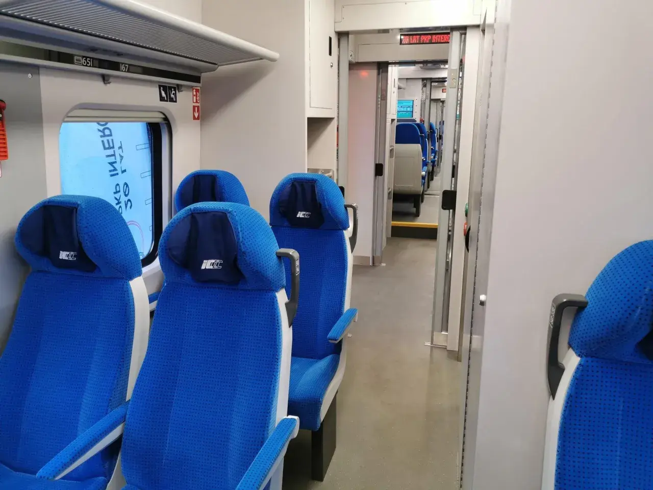 Wnętrze pociągu ed74 z niebieskimi siedzeniami i przejściem.