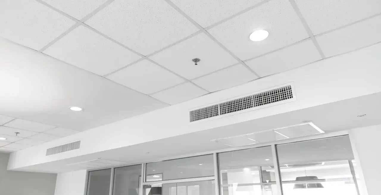 Soffitto modulare bianco con faretti, bocchette di ventilazione e un sistema di controsoffitto autoportante che nasconde gli impianti.
