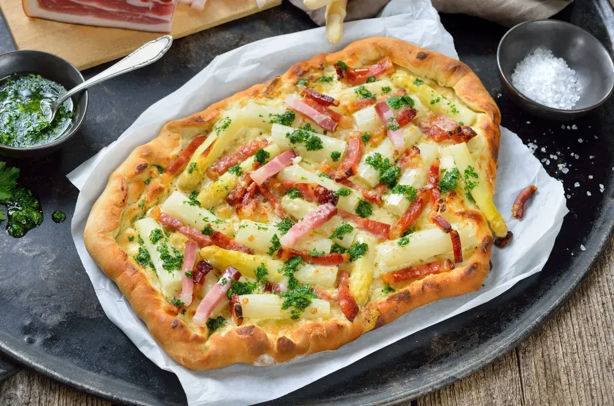 Pyszna pizza ze szparagami i boczkiem, posypana świeżą natką pietruszki. Idealna na wiosenny obiad.
