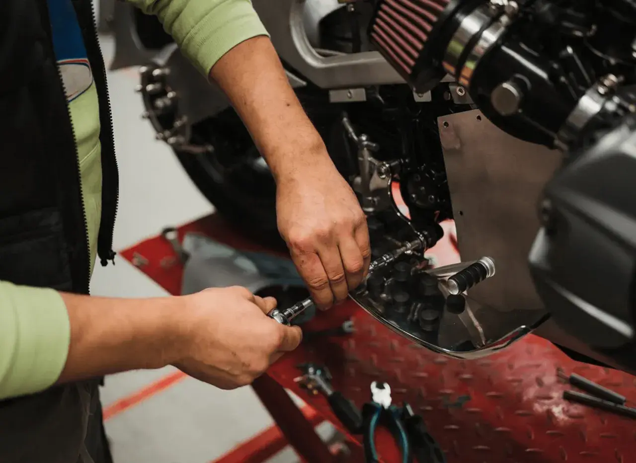 Mecánico realizando el cambio de aceite a una moto, usando herramientas para acceder al motor.