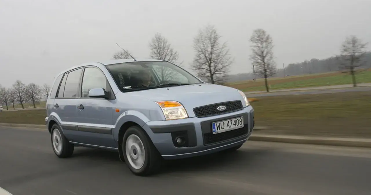 Jasnoszary Ford Fusion 1.4 benzyna jedzie po drodze. W tle drzewa i pola.