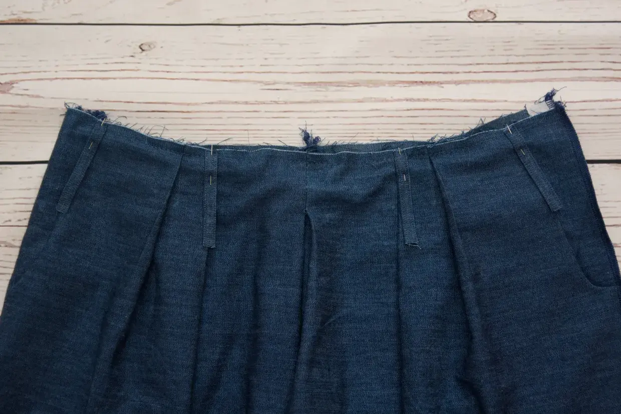 Close-up of a denim garment's waistband, showcasing various types of belt loops being prepared for sewing.
